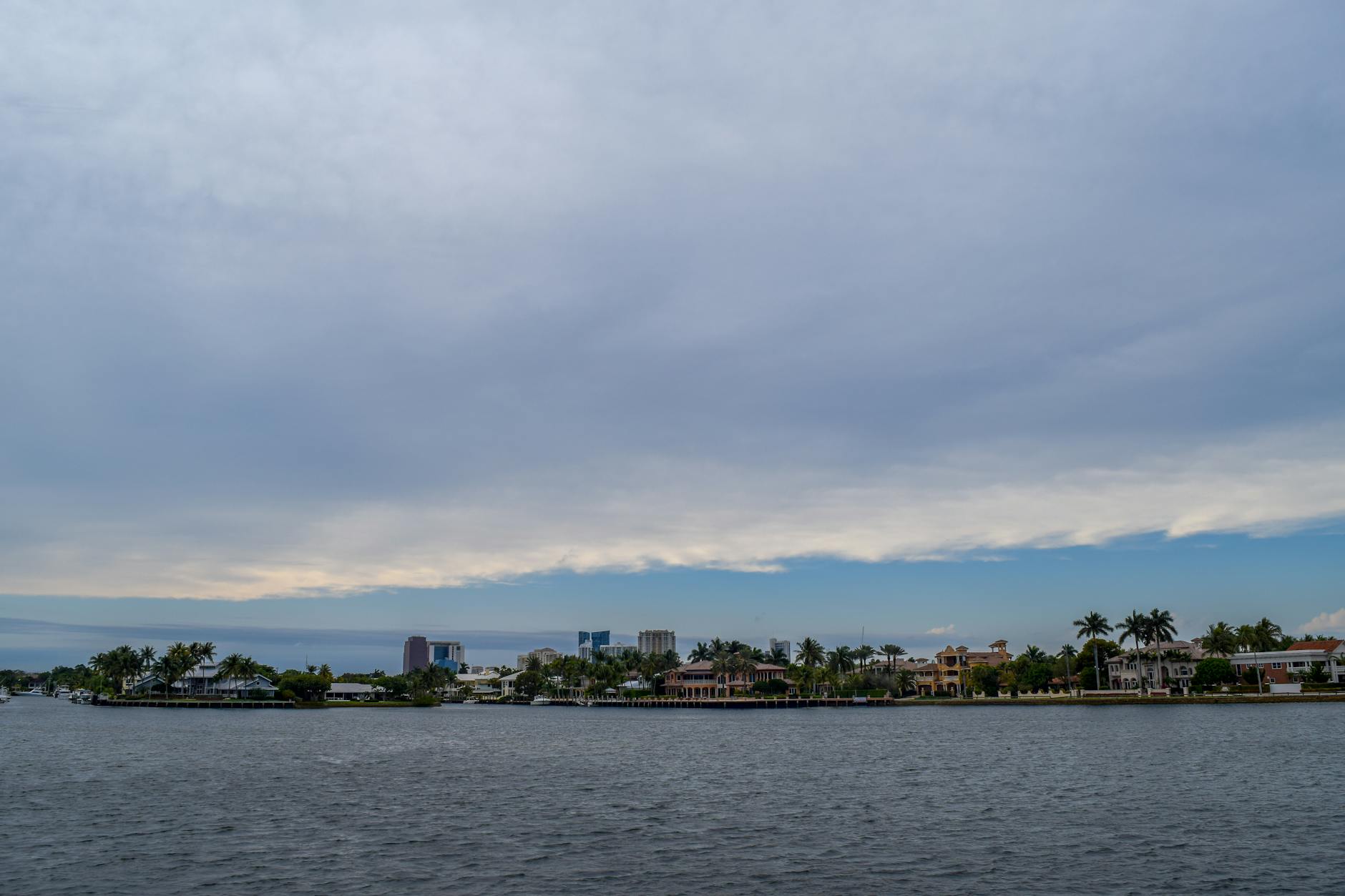 A tranquil coastal scene with tropical waterfront houses and palm trees under a cloudy sky.
