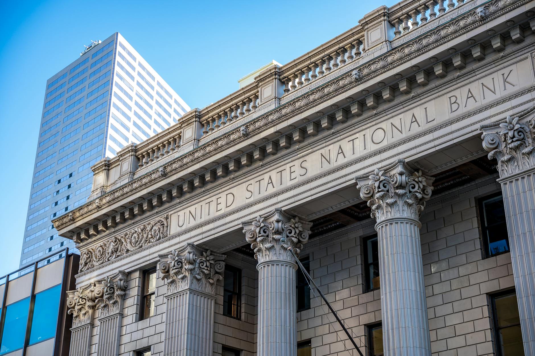 Exterior of historic national bank with decorative elements on classic columns located in city with modern building against blue sky