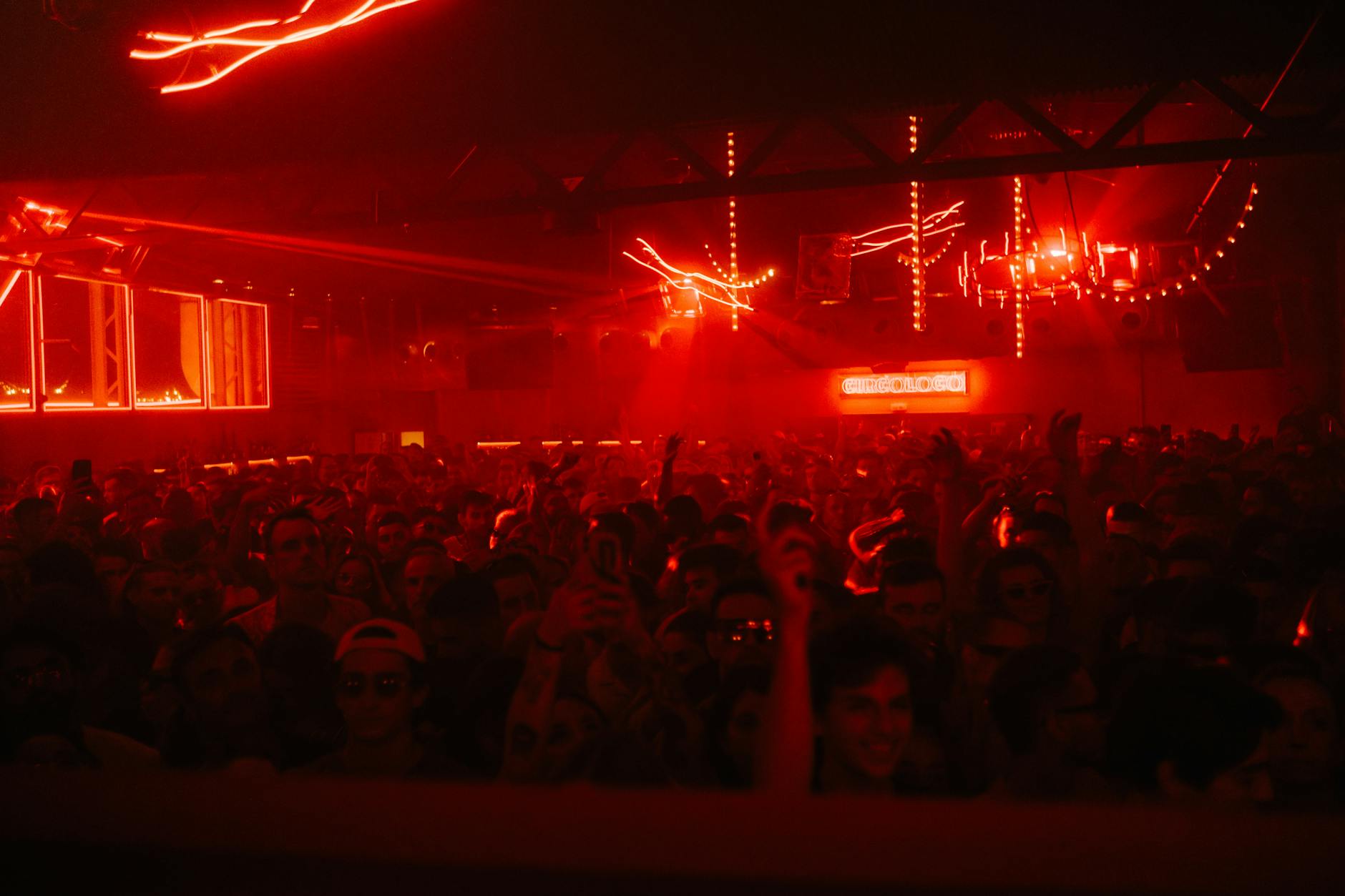 A packed nightclub with a vibrant atmosphere, red lights, and dancing crowd.
