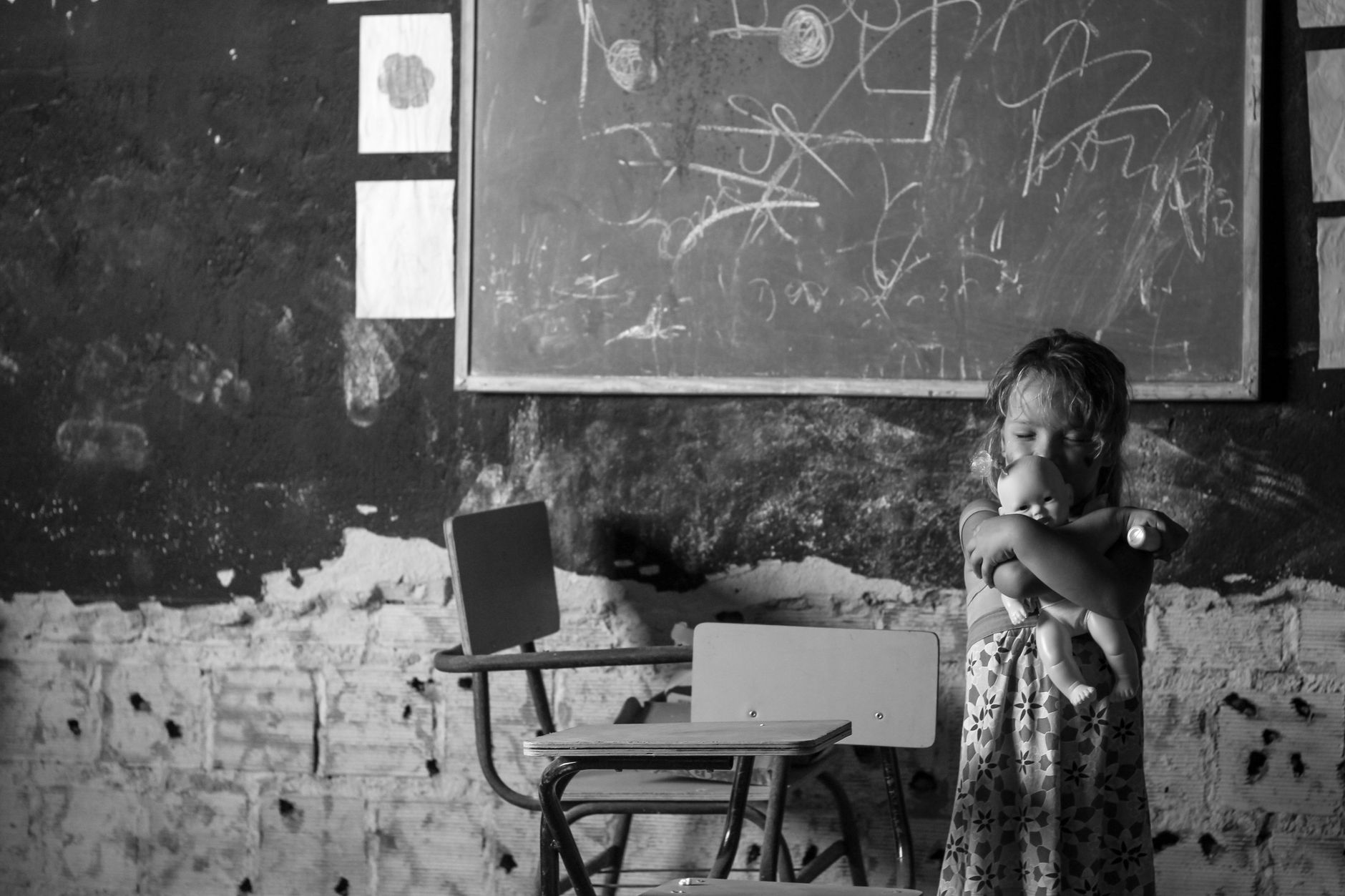A young girl hugging a doll in a vintage classroom, evoking nostalgia.