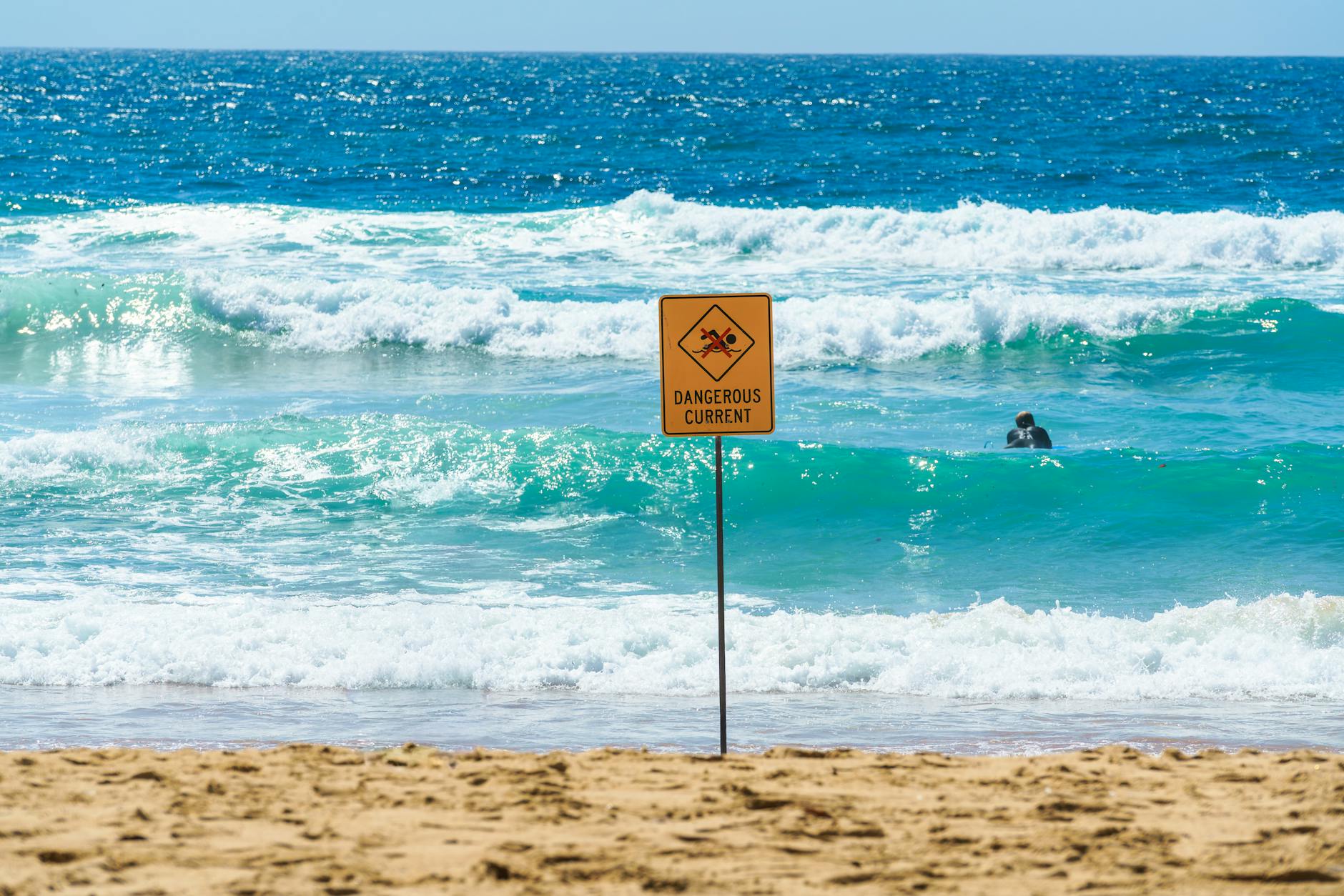 Beach scene with ocean waves and a warning sign for dangerous currents in Australia.